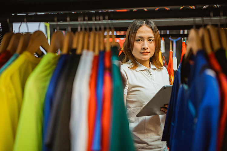Woman holding a tablet looking through customized sports jerseys. 